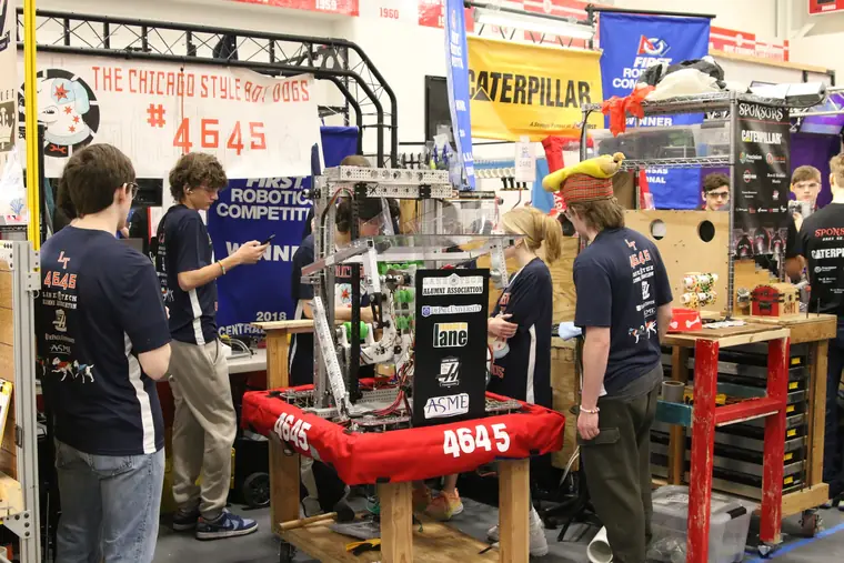 Team 4645 members working on their competition robot in the pit area at a FIRST Robotics event.